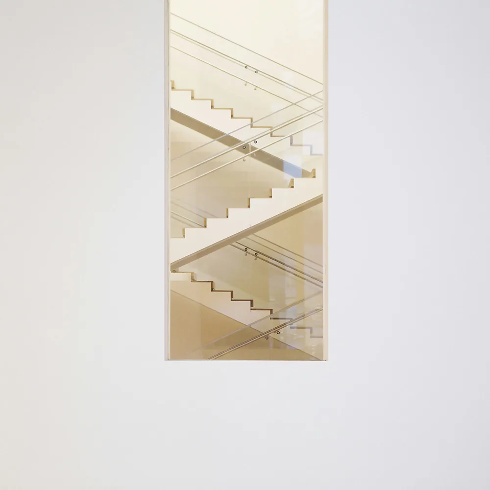 Escalier minimaliste blanc au finition épuré vue à travers d'une fenêtre rectangulaire mise verticalement.